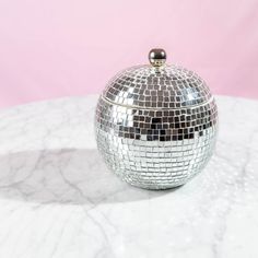 a silver disco ball sitting on top of a white marble table next to a pink wall