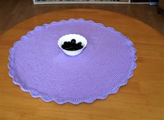 a crocheted placemat on a table with a bowl of black stones in it