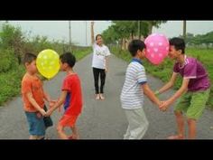 a group of children walking down a road with balloons on their heads and two adults holding hands