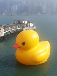 an inflatable rubber duck floating on the water next to a pier and buildings