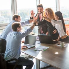 group of business people giving high fives to each other in an office meeting room