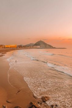 the sun is setting at the beach with people walking in the water and on the sand