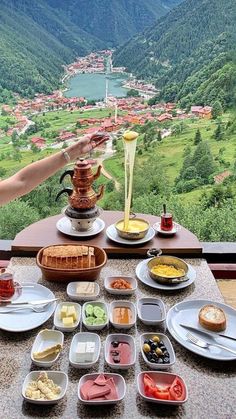 a table topped with plates and bowls filled with food next to a scenic valley below