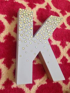 the letter k is decorated with sequins and sits on a red carpeted surface