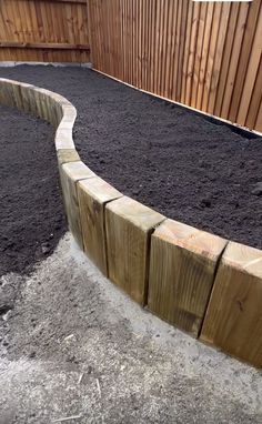 a wooden retaining wall in the middle of a graveled area next to a fence