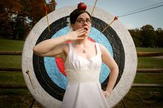 a woman standing in front of a target with an apple on her head and two arrows sticking out of her mouth