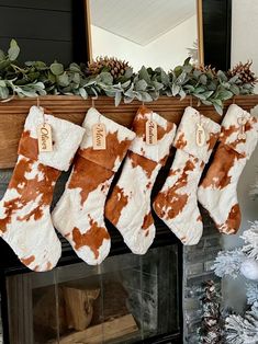 christmas stockings hanging from a mantel decorated with brown and white cow hides, along with greenery