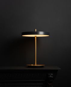 a black table with a gold base and a light on it in front of a dark wall