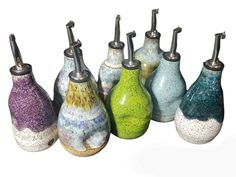 seven vases are lined up in different colors and sizes, each with a unique design