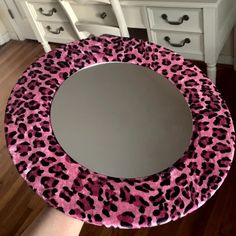 a pink and black leopard print mirror sitting on top of a wooden floor next to a white dresser