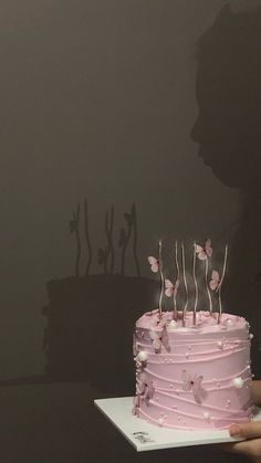 a person holding a cake with pink icing and butterflies on it in front of a dark background