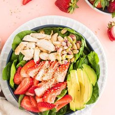 a salad with strawberries, avocado and chicken on it next to two bowls of strawberries