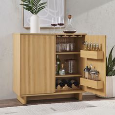 a wooden cabinet with wine glasses and bottles in it next to a potted plant