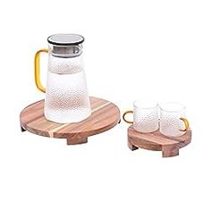 a pitcher and two mugs on a wooden coaster with one glass in the middle