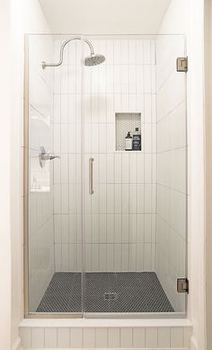 a walk in shower sitting next to a white tiled wall and floor with a glass door