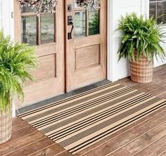 two potted plants sitting on the front porch next to an entry mat and door