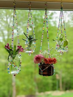 three hanging planters filled with flowers on a window sill in front of a tree