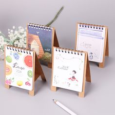 three desk calendars sitting on top of each other next to a pen and flower