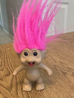 a toy troll with pink hair on top of a wooden table