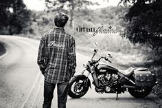 a man standing next to a motorcycle on the side of a road with trees in the background