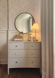 a white dresser with a mirror on top of it next to a lamp and window