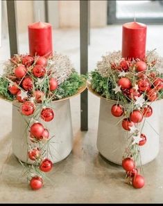 two red candles sitting on top of white buckets filled with christmas balls and greenery