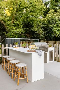 an outdoor kitchen with bar stools next to it and trees in the back ground