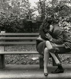 a man and woman sitting on a bench in front of a tree hugging each other