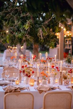 a table set up for a formal dinner with candles and flowers in vases on the tables