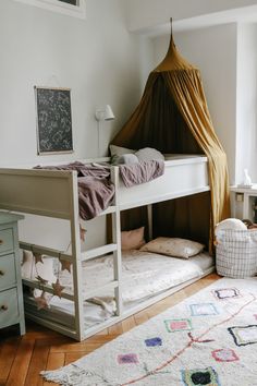 a white bunk bed sitting in a bedroom next to a dresser and rug on top of a hard wood floor