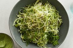 a bowl filled with shredded green vegetables next to a small bowl of pesto sauce