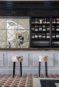 two chairs sitting in front of a bar with bottles on the wall and flooring