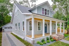 a small house with white siding and blue door on the front porch, surrounded by trees