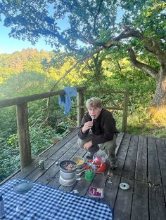 a man sitting on a wooden deck next to a picnic table with food and drinks