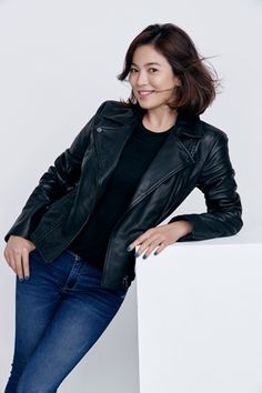 a woman in black jacket and jeans leaning against a wall