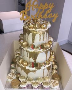 a three tiered cake is decorated with gold and white icing, topped with chocolate covered cupcakes