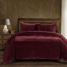 a bed with a maroon comforter and pillows