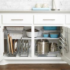 an open cabinet with pots and pans on the bottom shelf in a white kitchen