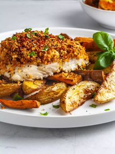 a white plate topped with fried fish and veggies next to a bowl of potato wedges