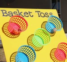 a basket toss game set up in front of a yellow sign with four different colored baskets on it