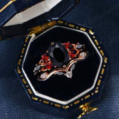 a black diamond ring with red and white stones in it's case on top of a blue cloth