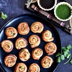 a black plate topped with small pastries on top of a blue table next to green sauce