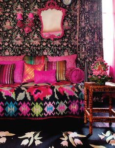 a bed with pink and green pillows on top of it next to a table in front of a window