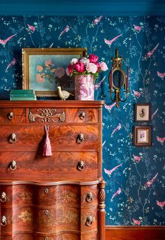 an old dresser with pink flowers on top and blue wallpaper behind it in a living room