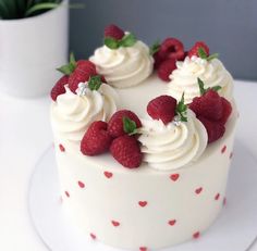 a white cake with raspberries and cream frosting on top sitting on a plate next to a potted plant