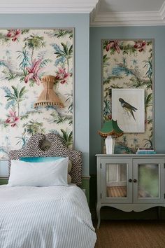 a bedroom decorated in blue and white with tropical wallpaper on the walls, bedding and nightstands