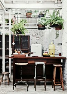 a table with two stools in front of it and some potted plants on the wall