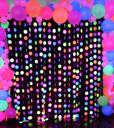 a black backdrop with neon colored balloons and streamers in the center is lit up at night