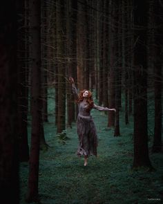 a woman is walking through the woods with her arms in the air