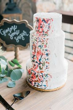 a wedding cake with flowers on it sitting on a table next to a chalkboard sign